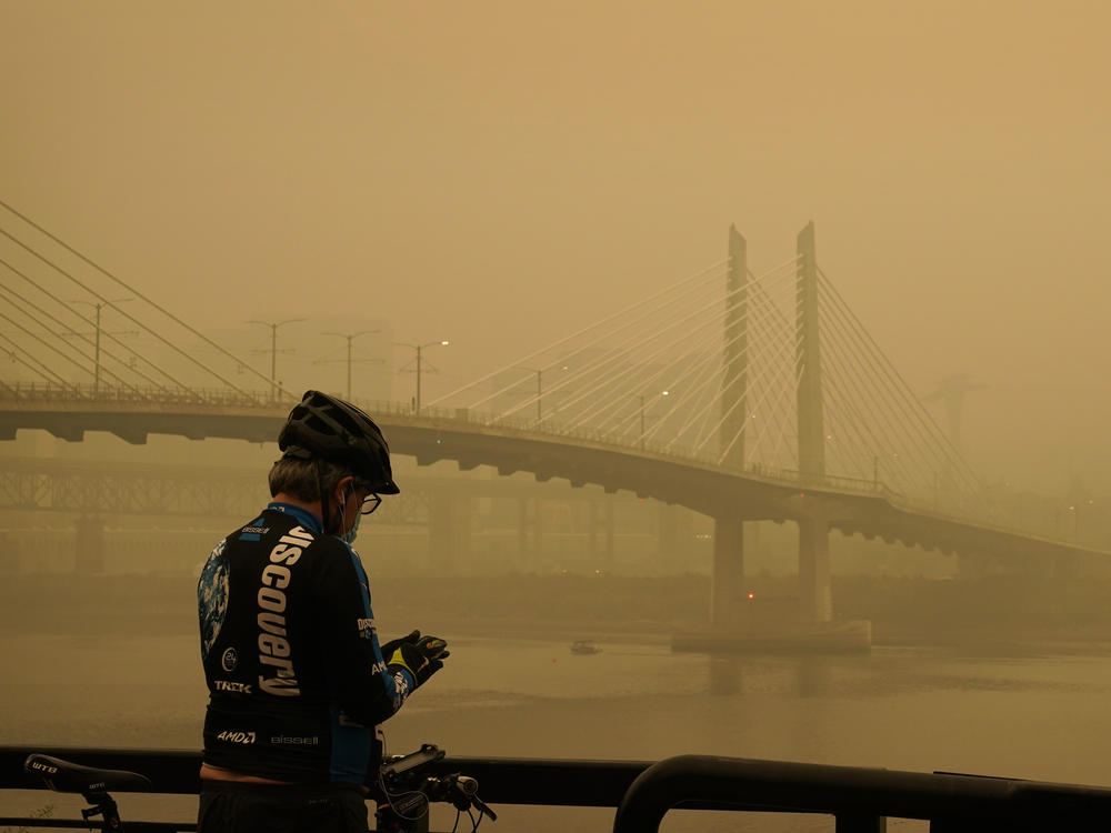 A man stops on his bike along the Willamette River as smoke from wildfires partially obscures the Tilikum Crossing Bridge on Saturday in Portland.