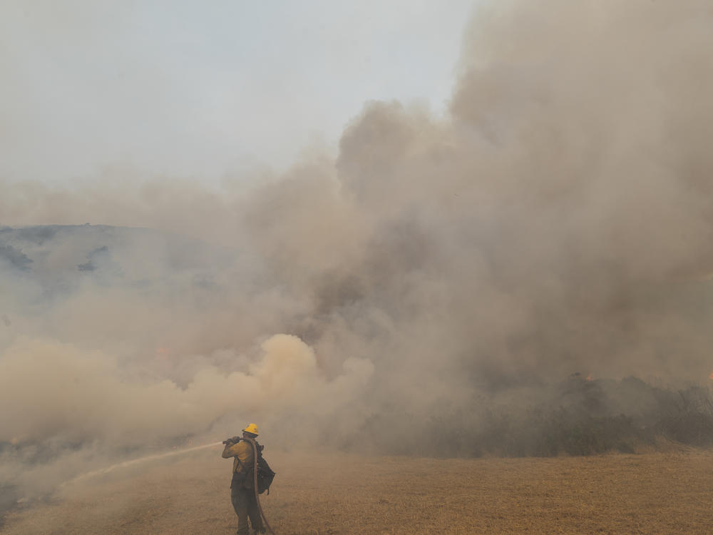A firefighter sprays water on a controlled burn Sunday while fighting the Dolan Fire near Big Sur, Calif. Millions of acres have burned in California and neighboring states this year.