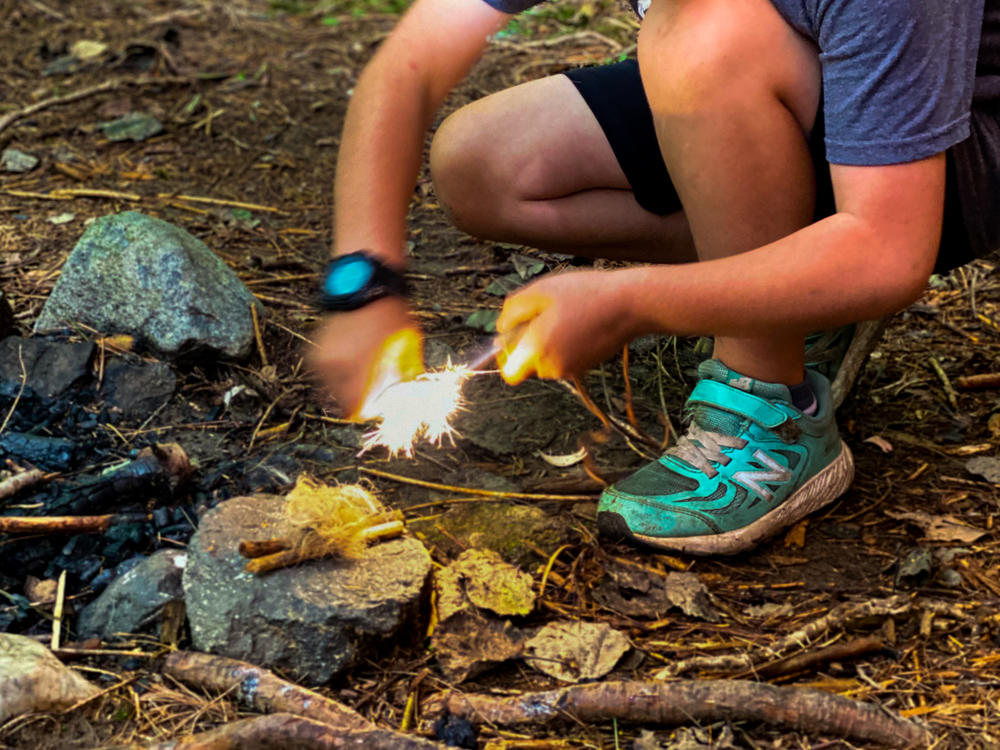Asher Wool, 8, uses a ferro rod and striker to light a bundle of tinder aflame at Earthwork school in western Massachusetts.