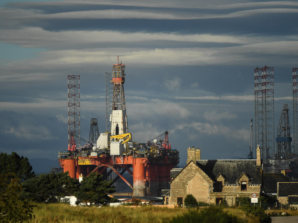 An oil rig towers over houses last week in Nigg, Scotland. Major players in the oil industry expect depressed oil demand and low prices to continue well into next year.
