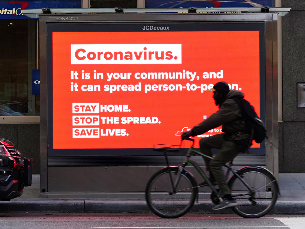 A person on a bike rides by a sign in New York City urging people to stay home in May. As the pandemic drags on, some workers are facing tough choices — balancing potential risks of unwittingly spreading the disease against the possibility of losing pay during a quarantine.