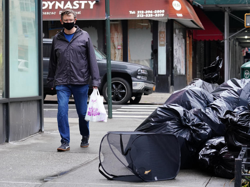 A man wearing a protective mask looks at piled-up trash in New York City on April 24. Cities are struggling with collection as the volume of residential garbage surges during the stay-at-home era.