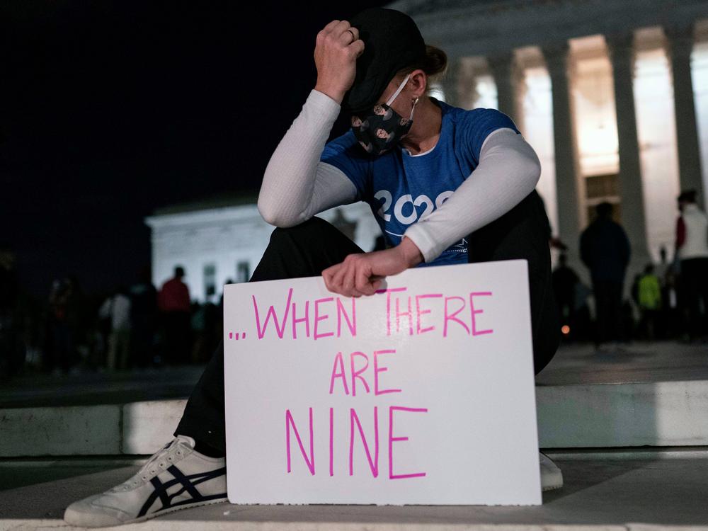 A woman, mourning the death of Ruth Bader Ginsburg, holds a sign at the Supreme Court that reads, 