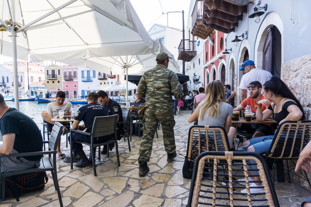 A Greek soldier walks past patrons sipping iced coffee at cafes in Kastellorizo's port.