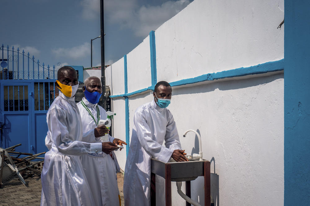 At the Celestial Church of Christ, church leaders guide a member to a handwashing station. When churches reopened earlier this year as Nigeria entered a new phase in its lockdown, they were instructed to provide worshippers with hand sanitizers and to ensure face masks are worn — even during services. <em>August 9. Lagos, Nigeria.</em>