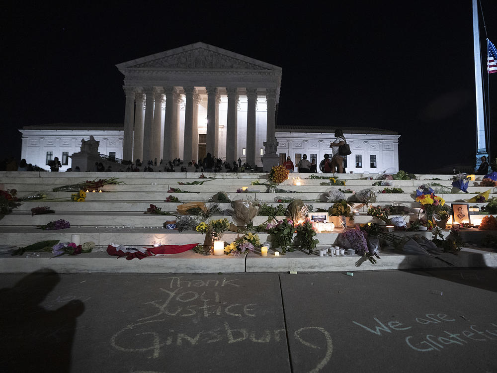 The national flag flies at half staff as people gather to mourn the passing of Supreme Court Justice Ruth Bader Ginsburg at the steps in front of the Supreme Court.