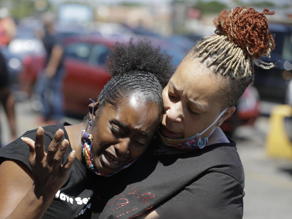 Two women pray in Louisville, Ky., in early June near the intersection where David McAtee was killed. Louisville police say video obtained from security cameras at McAtee's barbecue restaurant and an adjoining business show that McAtee fired a gun as police and National Guard soldiers were enforcing a curfew approached his business.