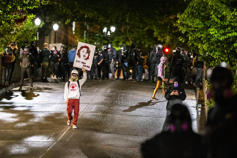 A protester walks toward Portland police with a sign honoring Breonna Taylor on Wednesday in Portland, Ore.