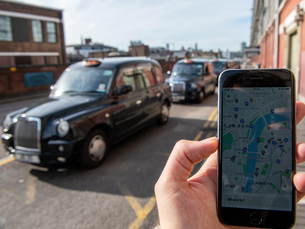 A phone shows the Uber app in front of a taxi stand at Waterloo station in London on Monday. The ride-sharing service won its appeal after Transport for London denied a renewal of its operating license late last year.