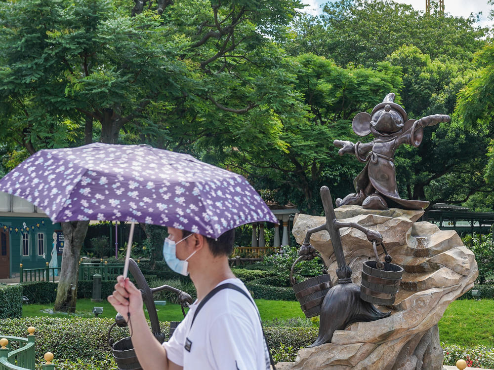 A visitor wears a mask while walking by Mickey Mouse at Hong Kong Disneyland.