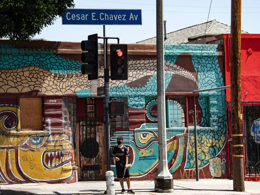 A man waits to cross the street in the largely Latino neighborhood of East Los Angeles on Aug. 7. California has implemented a new health equity metric to help address the outsize effect of coronavirus on the state's communities of color.