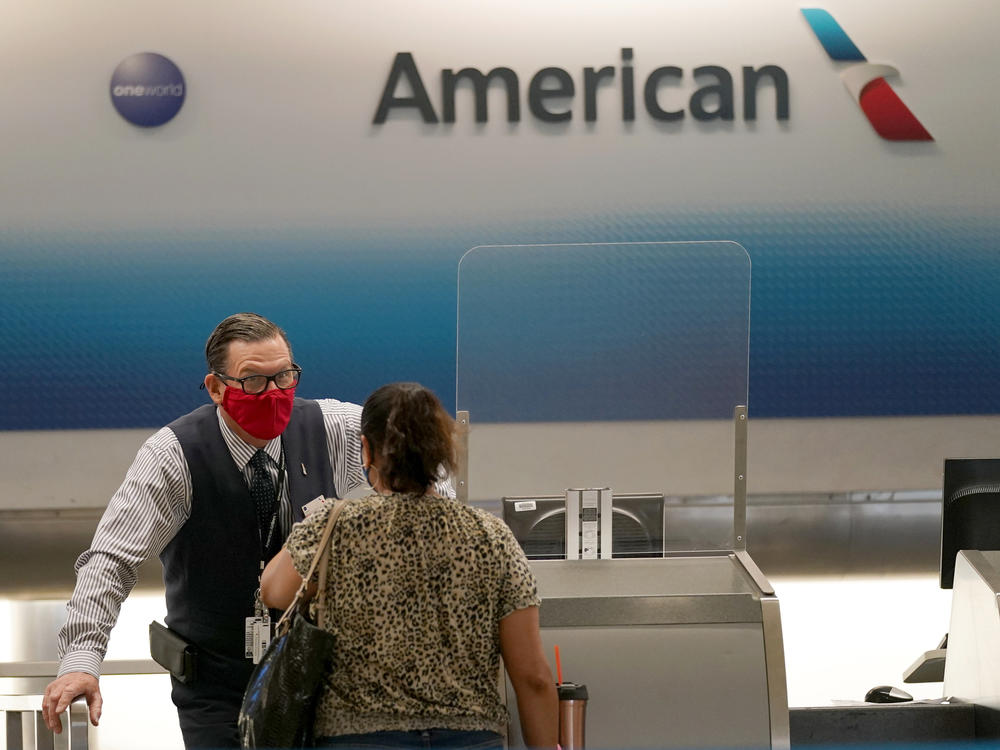 American Airlines ticket agent Henry Gemdron, left, works with a customer at Miami International Airport on Sept. 30. Travel industry groups warn of huge job losses if Congress and the White House fail to reach agreement on coronavirus relief soon.