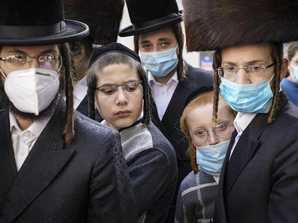 Members of the Orthodox Jewish community gather around a journalist as he conducts an interview on a street corner, last Wednesday, in the Borough Park neighborhood of the Brooklyn borough of New York. Gov. Andrew Cuomo moved to reinstate restrictions on businesses, houses of worship and schools in and near areas where coronavirus cases are spiking.