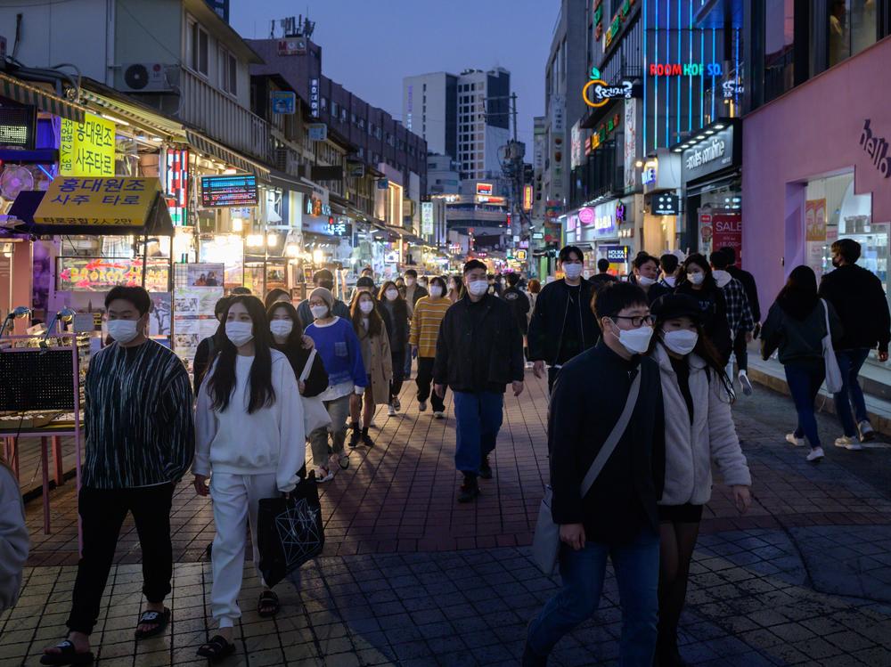 People wearing face masks walk on a street Sunday in the Hongdae district of Seoul, South Korea.