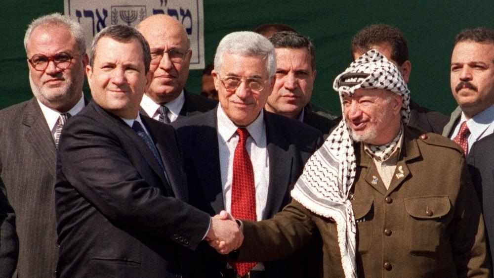 Chief Palestinian negotiator Saeb Erekat (farthest to the left), with Israeli and Palestinian officials as Israeli Prime Minister Ehud Barak (left) and PLO Chairman Yasser Arafat (right) shake hands before a summit at the Erez Crossing in the Gaza Strip in 2000.
