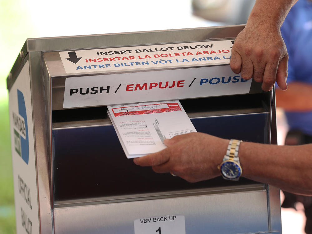 A poll worker places vote-by mail ballots into a ballot box this month at the Miami-Dade County Election Department headquarters in Doral, Fla. Voters in Florida are among those who have reported receiving emails threatening them to vote for President Trump.