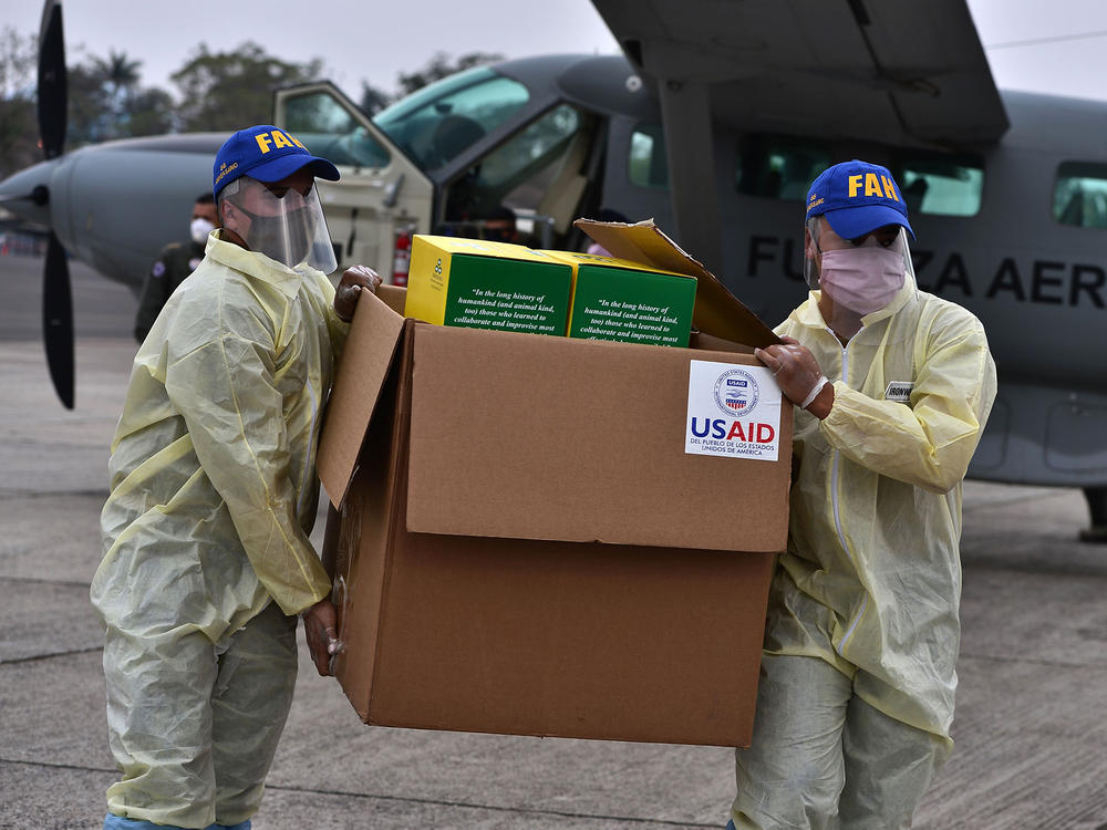 Foreign aid takes many forms — and Trump and Biden have differing perspectives. Above: Members of the Honduran Armed Forces carry a box of COVID-19 diagnostic testing kits donated by the United States Agency for International Development and the International Organization for Migration.