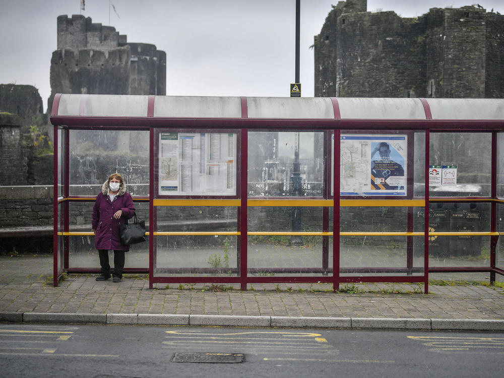 A woman wears a face mask as she waits for a bus last month in South Wales. Wales is imposing a lockdown amid a surge in cases.