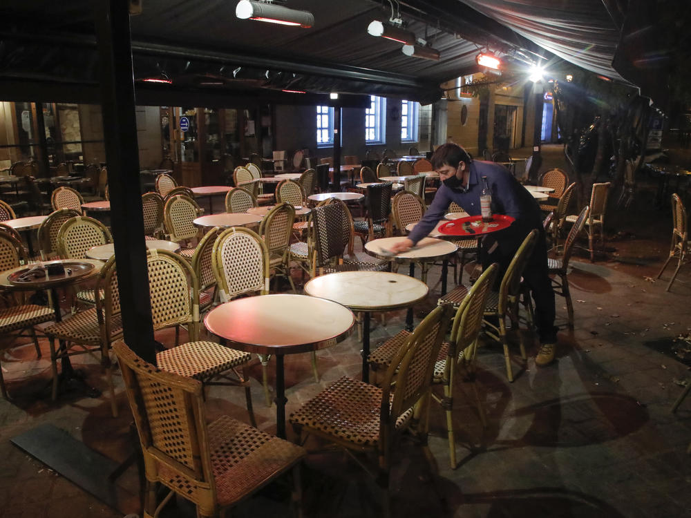 A waiter cleans a table this month after closing in St. Germain-en-Laye, west of Paris, to comply with COVID-19 restrictions forcing restaurants in the French capital to close. France has imposed a nighttime curfew in Paris and other major cities to curb the spread of the coronavirus.