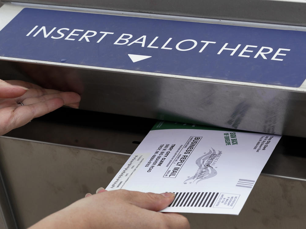 A voter is shown inserting her absentee voter ballot into a drop box earlier this month in Troy, Mich. A Michigan judge has blocked a ban on openly carrying guns in polling places on Election Day.
