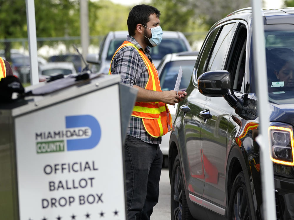 An election worker takes ballots from voters dropping them off at an official ballot drop box this week at the Miami-Dade County Board of Elections in Doral, Fla.