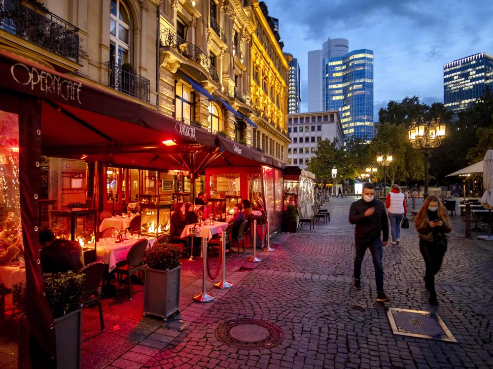 People wearing face masks walk past an outdoor restaurant Wednesday in Frankfurt, Germany. To slow the spread of the coronavirus, restaurants will be closed, starting Monday.