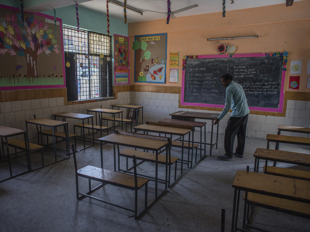 An employee adjusts desks in an empty classroom in New Delhi after schools there were closed in March. A new report finds 1 in 4 countries have either missed their planned school reopening date, or not yet set one.