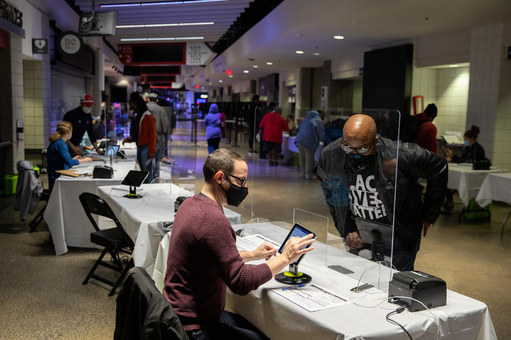 Brian Diem (left) checks in a voter on the first day of early voting at Capital One Arena in Washington, D.C., on Tuesday.