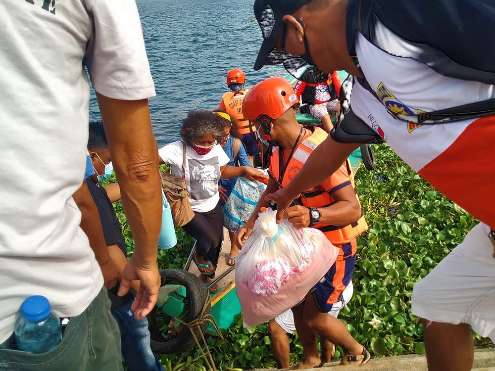 In this photo provided by the Philippine Coast Guard, families are evacuated by members of the Philippine Coast Guard to safer ground in Camarines Sur province as they prepare for typhoon Goni. Families living near coastal towns have moved to evacuation centers as the strong typhoon nears.