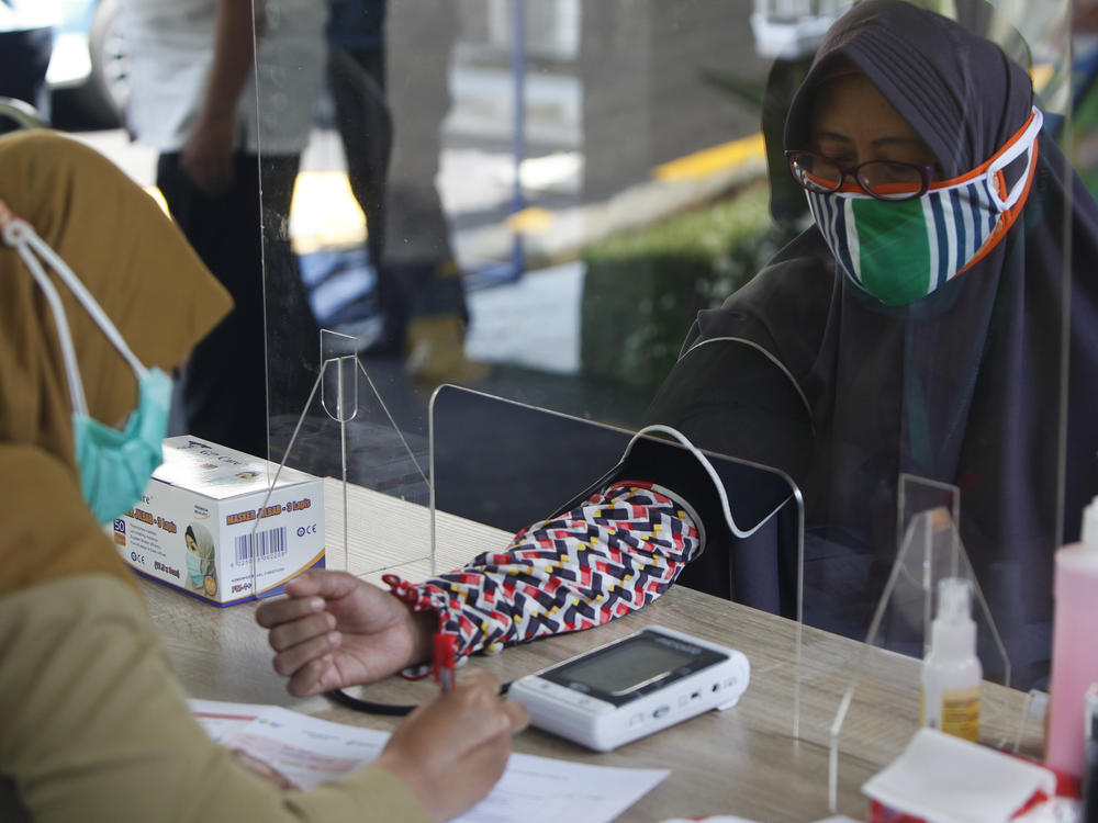 Health workers measure a woman's blood pressure during a simulation of a COVID-19 vaccine trial in Indonesia.