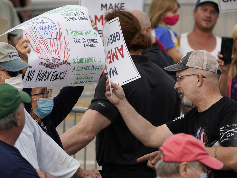 At a Saco, Maine, campaign rally for President Trump in September, a protester holding a sign detailing the effects of climate change on the Gulf of Maine (left) came face to face with Trump supporters who had different views.