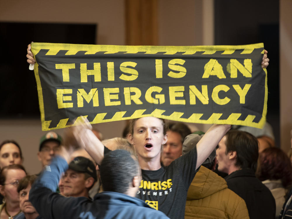 A climate change protester holds a banner reading, 