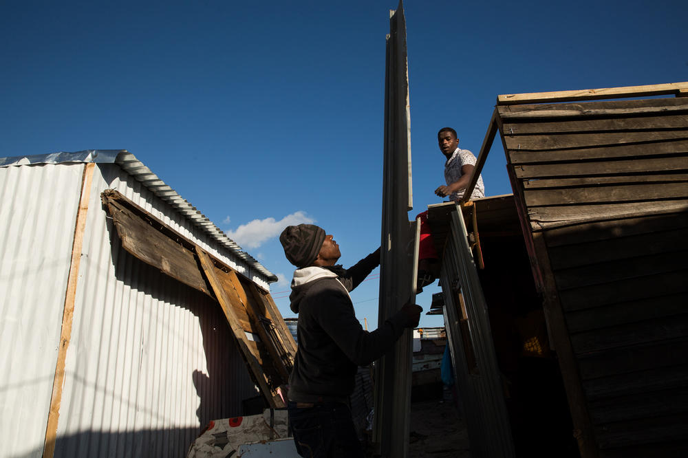 Two men help Noxolo Nondala build her home in Covid. She previously lived in the township of Khayalitsha, where she had been a backyard dweller, renting a structure that was literally in someone's backyard. Although she liked her life in Khayalitsha, she said she moved to Covid 