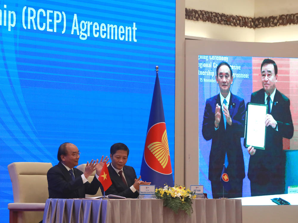 Vietnamese Prime Minister Nguyen Xuan Phuc (left) and Trade Minister Tran Tuan Anh applaud next to a screen showing Japanese Prime Minister Yoshihide Suga and Trade Minister Hiroshi Kajiyama holding up signed RCEP agreement, in Hanoi, Vietnam. China and 14 other countries have agreed to set up the trading bloc.