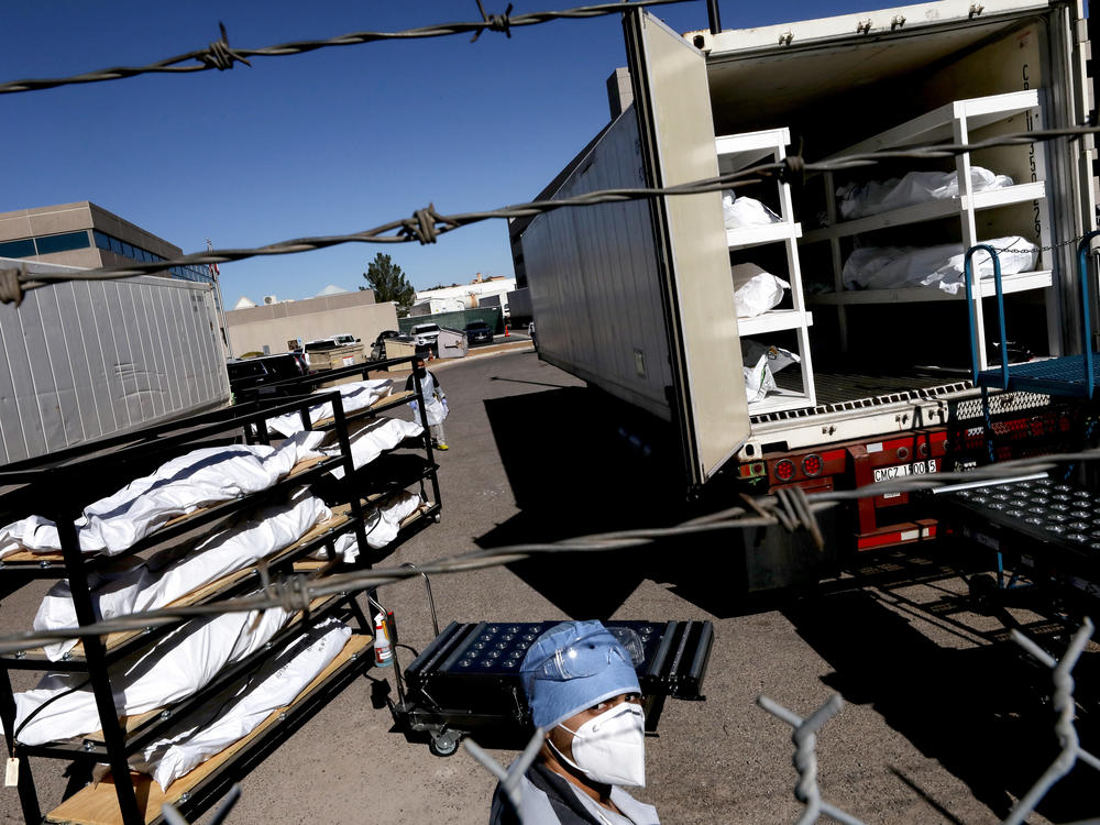 An inmate from the El Paso County detention facility prepares to load bodies wrapped in plastic into a refrigerated temporary morgue trailer.