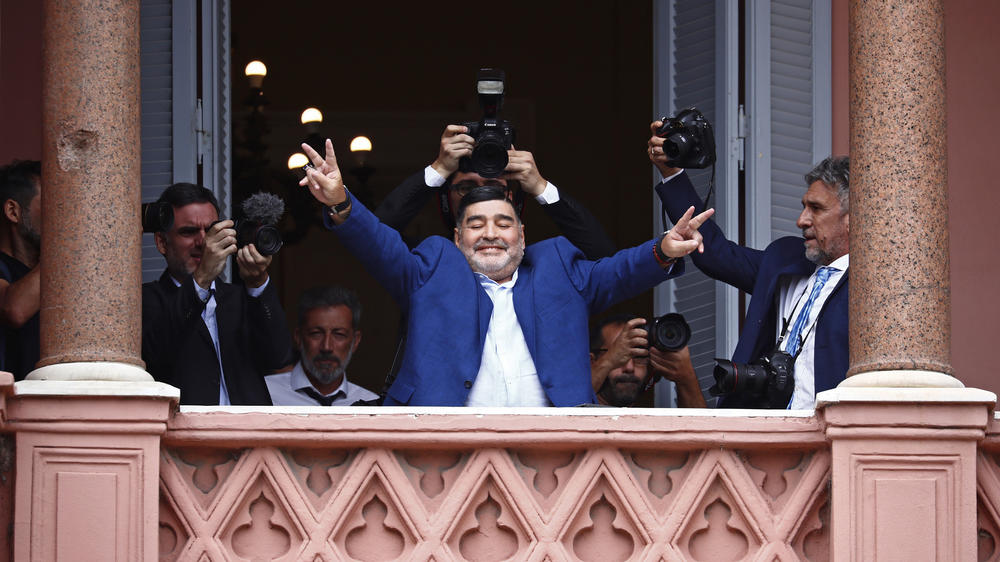 Soccer great Diego Maradona flashes victory signs to fans below at the Casa Rosada government house in Buenos Aires after meeting with Argentina's president last December. Maradona died Wednesday at age 60.