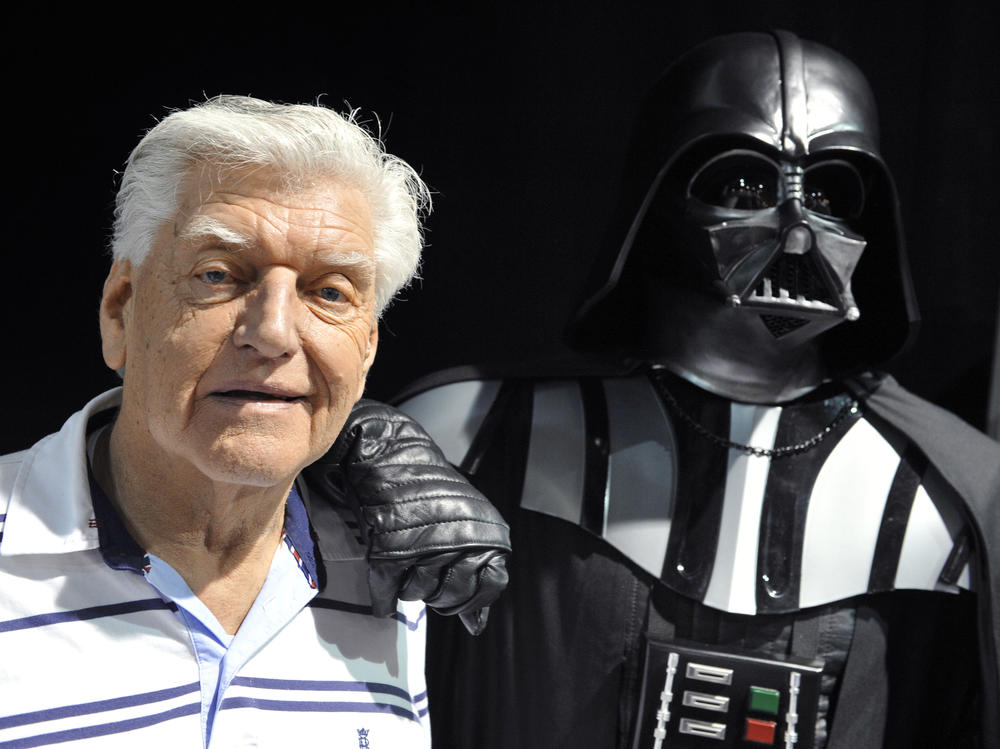 British actor David Prowse, who played Darth Vader in the first Star Wars trilogy, poses with a fan dressed in a Darth Vader costume during a Star Wars convention on April 27, 2013. On Sunday morning, Prowse's management company shared the news of his death at age 85.