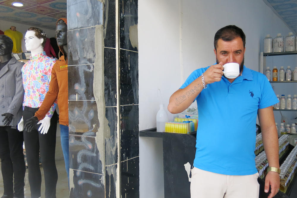 Ziyad Qirany, a Yazidi shop owner in Sinjar, returned three weeks ago and opened a small clothing store. No other shops are open yet on the street. The tattoo on his arm reads 2014-8-3, the date the ISIS genocide against Yazidis started six years ago.