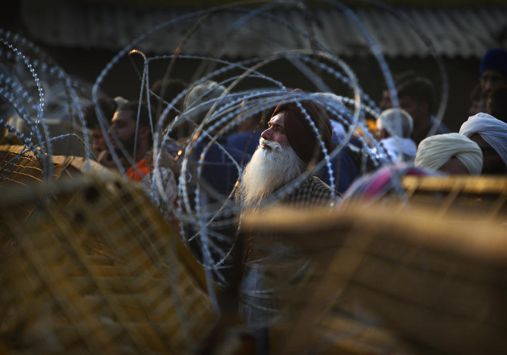 An Indian farmer looks through barbed wire that police put up at a protest site Thursday at the Delhi-Haryana state border.