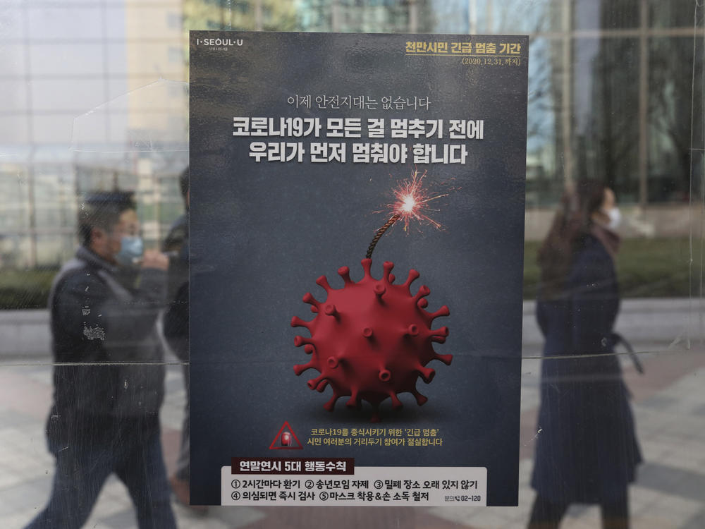 People wearing face masks as a precaution against the coronavirus pass by a poster emphasizing an enhanced social distancing campaign at a bus station on Monday in Seoul.