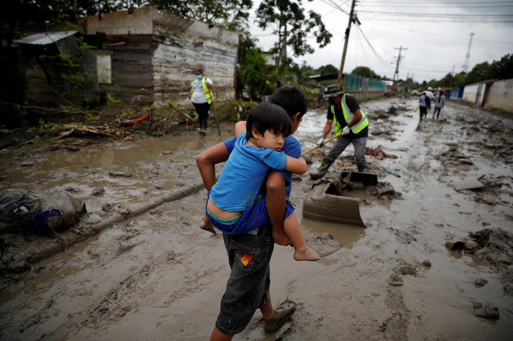 A child carries his brother down a street covered in mud after floods caused by hurricanes Eta and Iota.