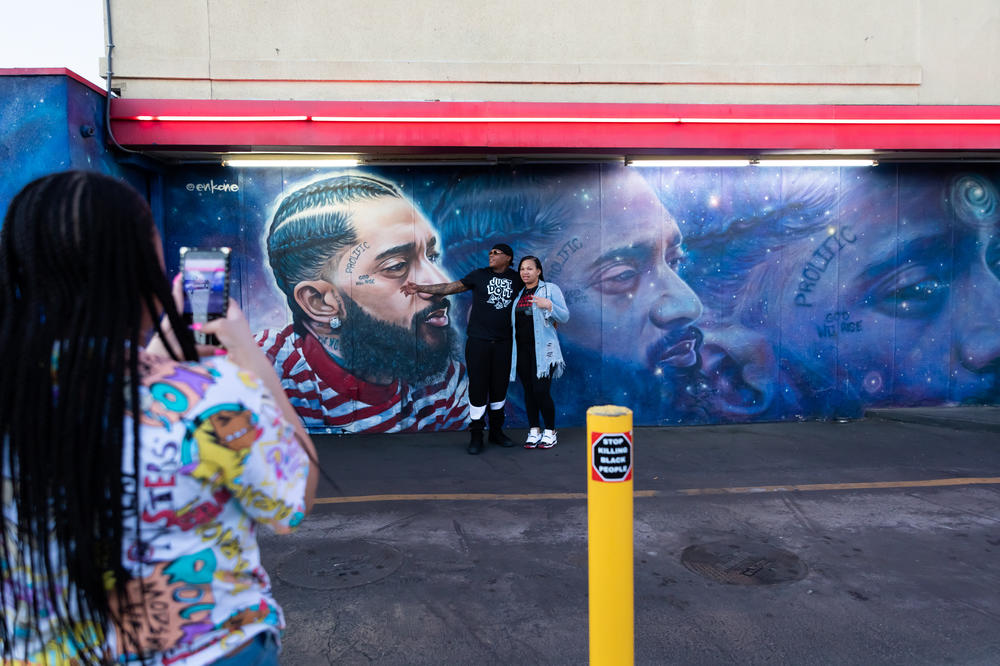 Bria Smith takes pictures of her parents Alexandria and Byron Smith in front of a Nipsey Hussle mural adorning the side of a FatBurger restaurant in Crenshaw. The visitors from Milwaukee got out to take photos while in line for food Dec. 5, 2020.