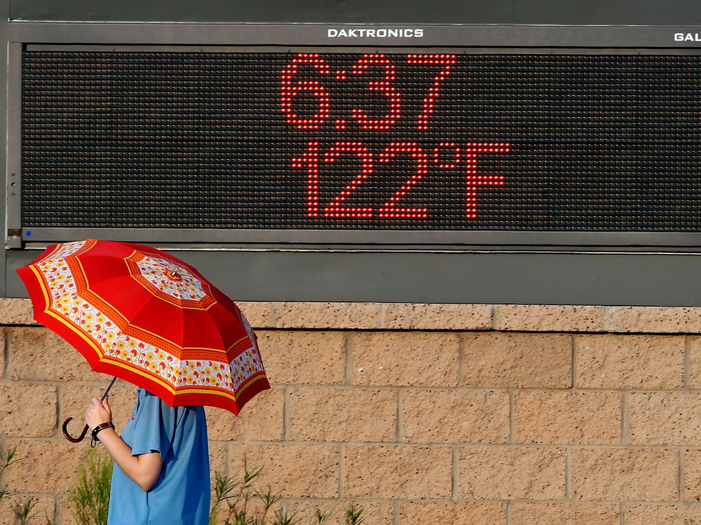 A pedestrian uses an umbrella to get some relief from the sun as they walk past a sign displaying the temperature on June 20, 2017 in Phoenix, Arizona. As 2020 comes to a close so does the hottest recorded decade.
