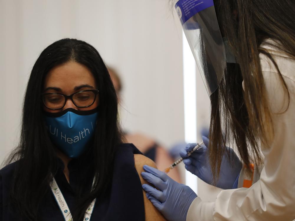 A doctor receives Chicago's first COVID-19 vaccination on Tuesday. In a new poll released the same day, respondents appeared to show less reluctance to receiving a coronavirus vaccine.
