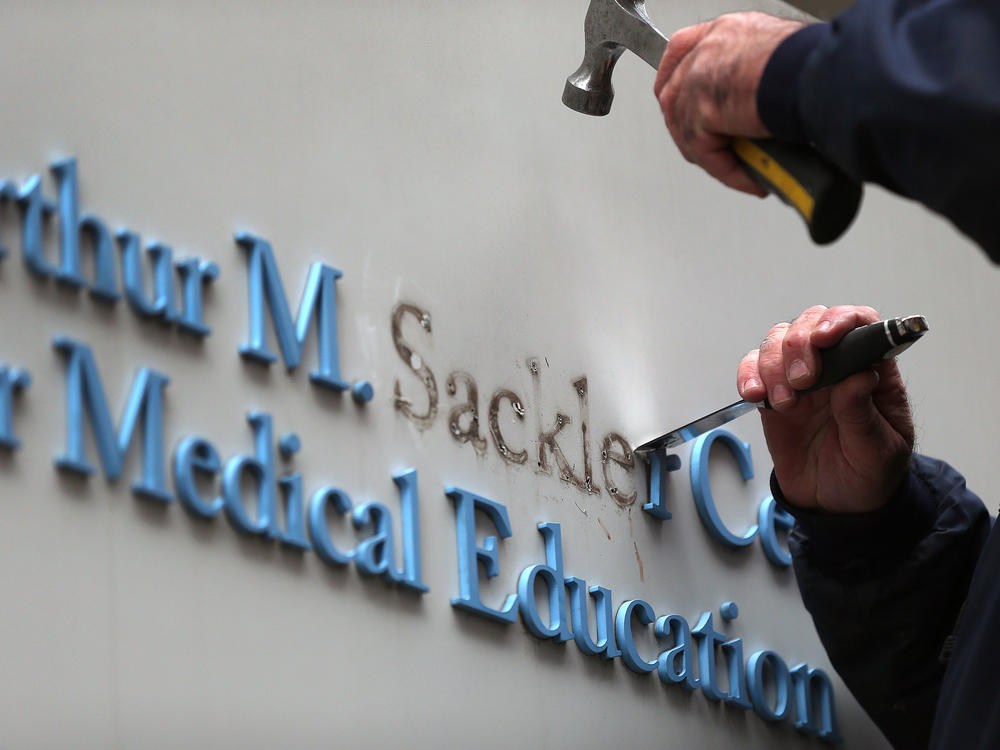 Tufts employee Gabe Ryan removes the Sackler family name from a building at Tufts University, the first major university to strip the Sackler name from buildings and programs.