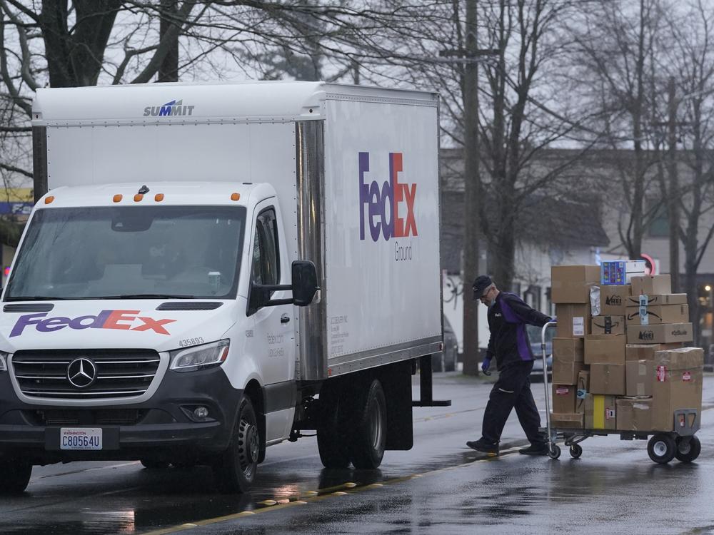 A driver with FedEx carries a package away from a van in Seattle. A huge increase in online shopping this year has demand for package delivery exceeding capacity this holiday season and stretching the delivery supply chain thin.
