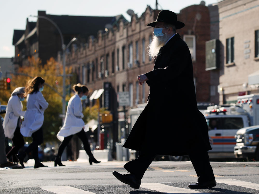 A Hasidic man and medical workers cross paths near the Maimonides Medical Center in Brooklyn, N.Y., in November. When public health messaging comes from community leaders, it's much more likely to be adopted, research on diverse groups finds.