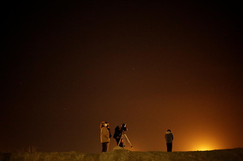 A family at the border crossing between Mexico and the U.S. in Ciudad Juarez uses a telescope to view Jupiter and Saturn during the Great Conjunction.