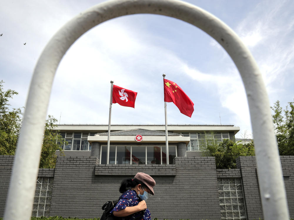 A woman wearing a face mask walks by the Government of Hong Kong Special Administrative Region office building in Beijing in June following the imposition of a national security law on Hong Kong. Ten Hong Kong fugitives were sentenced to prison Wednesday for illegally crossing international boundaries.