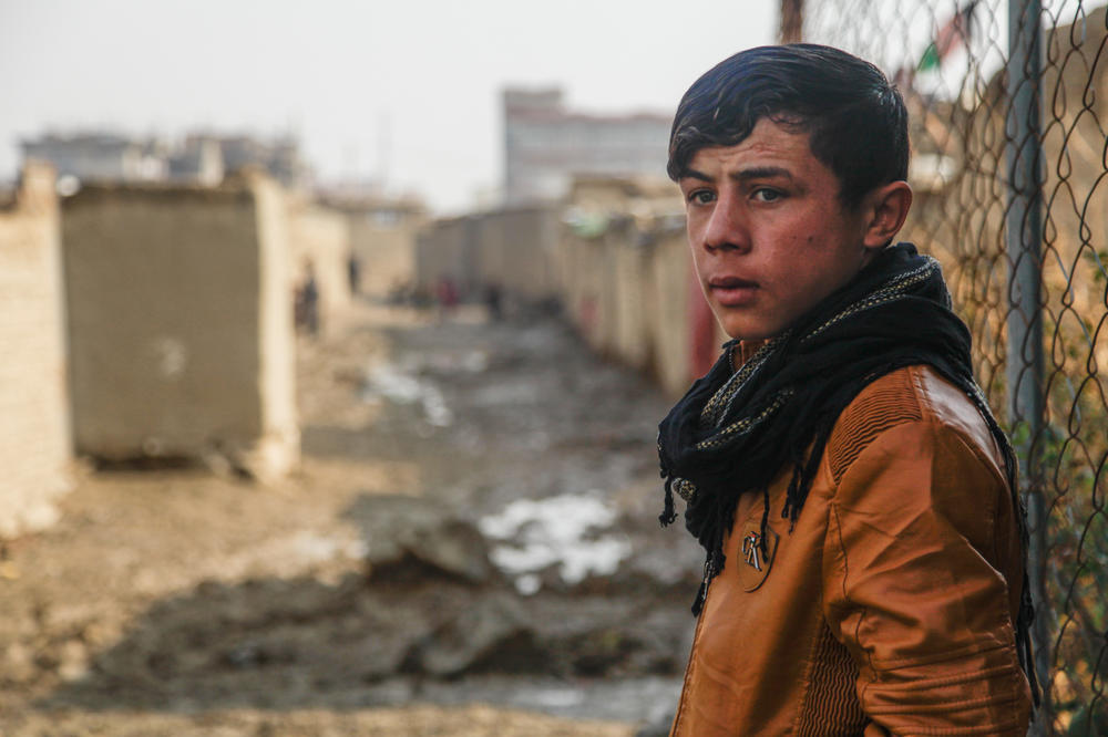 Shaista's 15-year-old son looks out onto a muddy alleyway on the outskirts of Kabul. He began selling firewood this year to help out his family after his father was injured in an accident.
